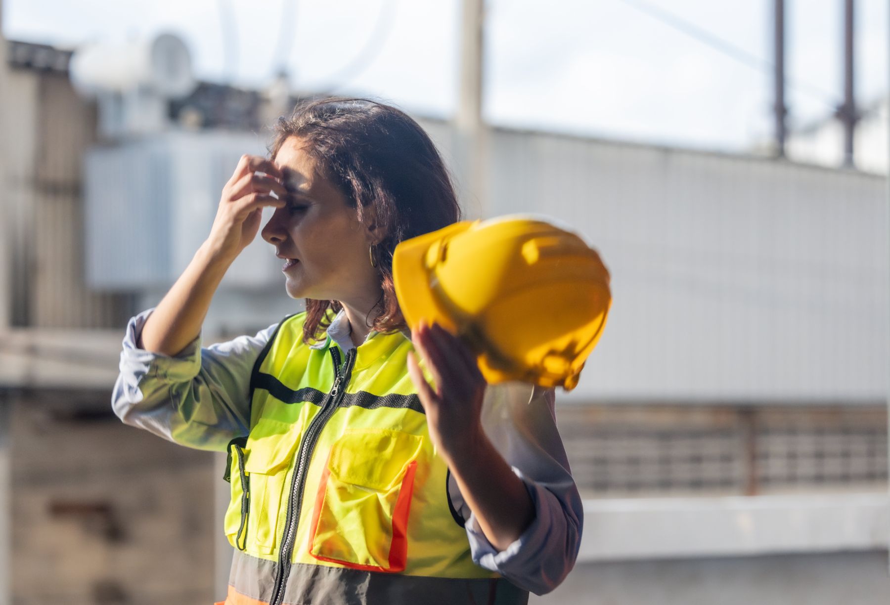 Construction worker in hi-vis holding her hard hat, looking stressed on site